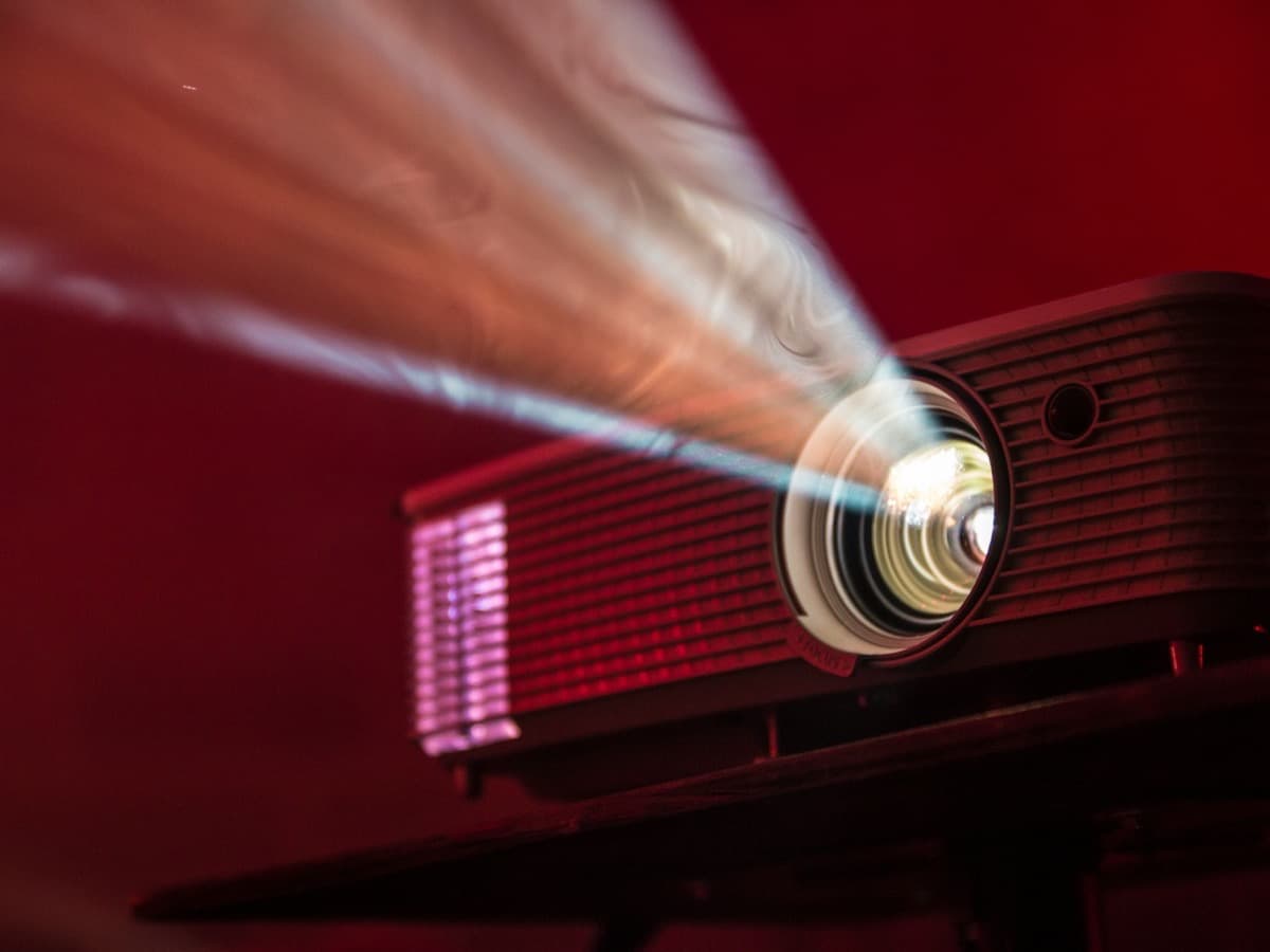 A projector on a stand throwing a bright beam of light across a dark red room.