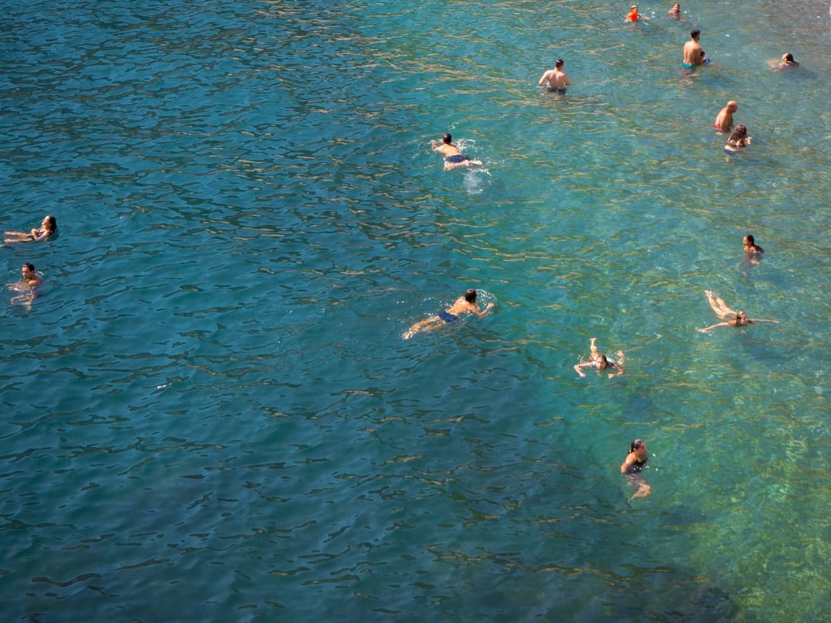 Swimmers spread out across clear blue-green open water, seen from above.