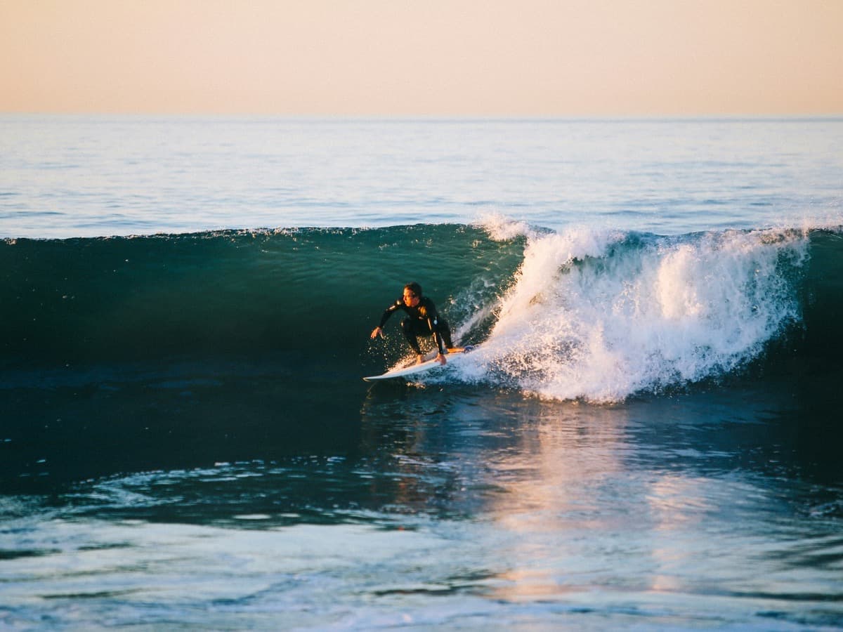 A surfer in a wetsuit riding along the face of a breaking wave in open sea.