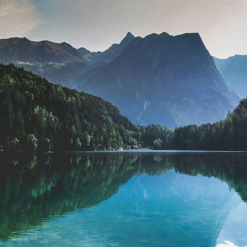 A still alpine lake reflecting a dark mountain ridge and forested slopes.